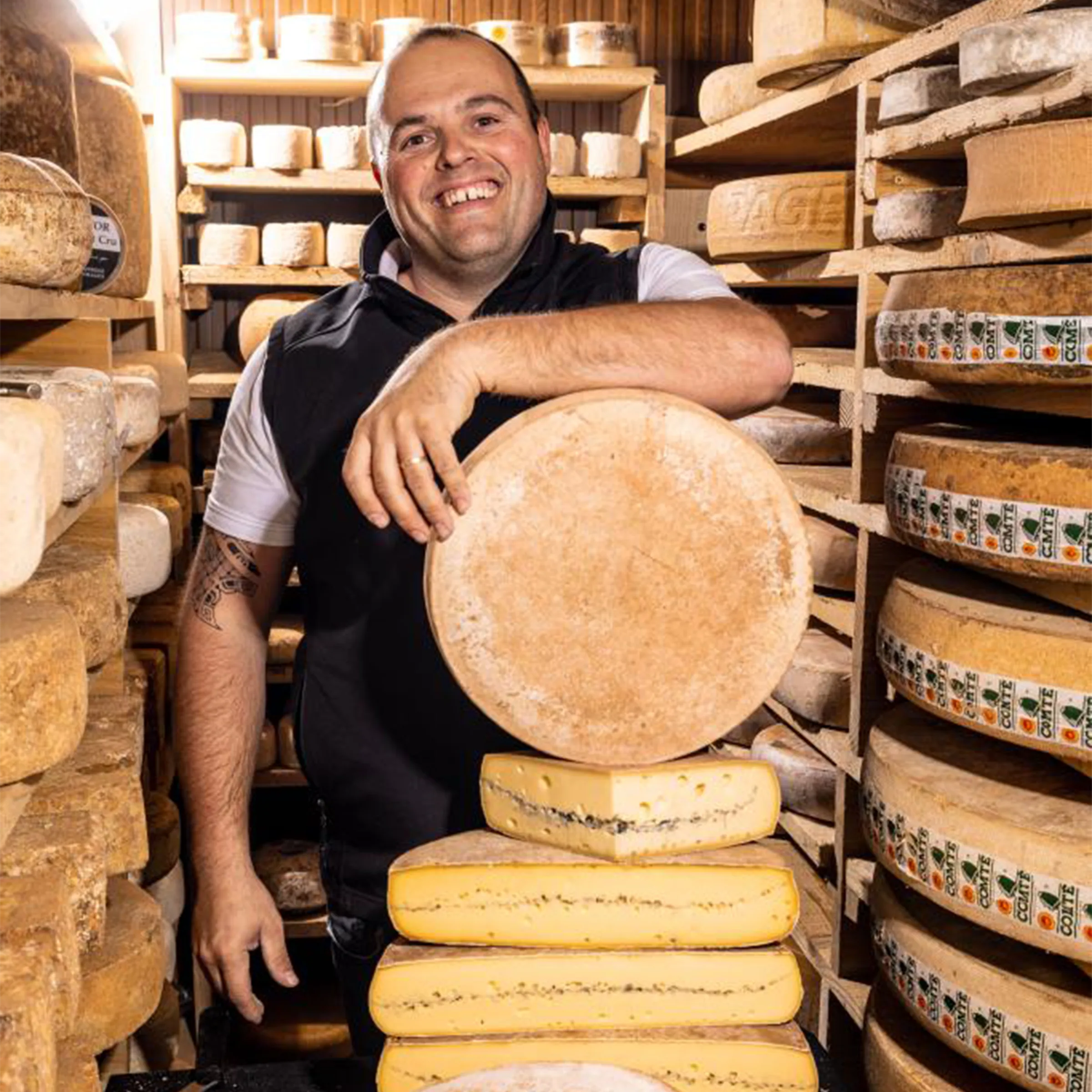 Freddy, fromager affineur, souriant au milieu des meules de fromage